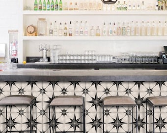 Puede incluir: Un mostrador de bar con un salpicadero de azulejos con estampado de estrellas blancas y negras. Tres taburetes de bar de metal negro están delante del mostrador.