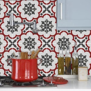 May include: Red and white kitchen tile backsplash with a black snowflake pattern. The tiles are arranged in a repeating pattern. A red pot with wooden utensils is on a hob in front of the tiles.