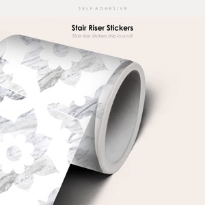 Könnte beinhalten: Eine Rolle selbstklebender Treppenstufenaufkleber mit weißem Hintergrund und einem grauen Marmormuster mit weißen Blumenmustern. Der Text "Stair Riser Stickers" und "Stair riser stickers ship in a roll" ist auf dem Etikett aufgedruckt.