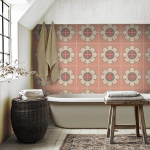 May include: A bathroom with a bath and a tiled wall. The tiles are peach coloured with a white and green floral pattern. There are towels on a stool and in a wicker basket.