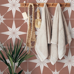 May include: Two beige towels hanging on a wooden rack against a wall with a terracotta background and white starburst tile pattern.