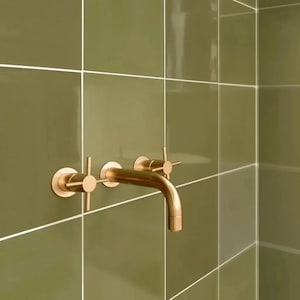 May include: A gold-toned bathroom faucet with two cross-shaped handles mounted on a green tiled wall.