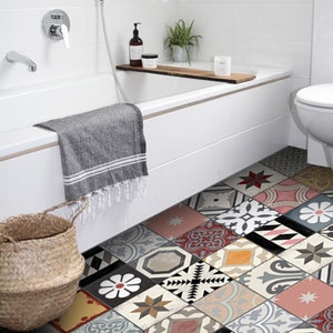 Può includere: Un bagno bianco con una vasca da bagno, un water e un pavimento piastrellato con un motivo. Il pavimento è composto da piastrelle di diversi colori, tra cui rosso, rosa, blu e giallo. C'è un asciugamano appeso sul lato della vasca da bagno.