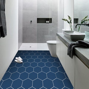 May include: A bathroom with a white toilet and a white vanity with a dark countertop. The floor is tiled with blue hexagonal tiles.
