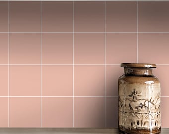 May include: A brown ceramic vase with a floral design sits on a light brown countertop in front of a wall of pale pink square tiles.