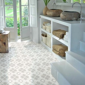 May include: A white bathroom with a patterned tiled floor, a white shelving unit with towels and baskets, and two stone sinks on a white countertop.