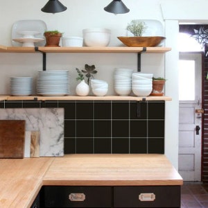 Puede incluir: Una cocina con un salpicadero de azulejos negros, estantes de madera y una encimera de madera. Los estantes están llenos de platos blancos, cuencos y plantas.
