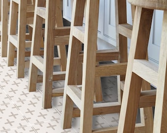 Könnte beinhalten: Eine Reihe von Barhockern aus Holz mit einer hellen Holzoptik. Die Hocker sind in einer Reihe angeordnet, wobei die Vorderseite der Hocker zum Betrachter zeigt. Die Hocker stehen auf einem weißen Fliesenboden mit einem braunen Kreuzmuster.