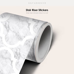 Könnte beinhalten: Eine Rolle selbstklebender Treppenstufenaufkleber mit einem weißen Marmor- und geometrischen Muster. Der Text "Stair Riser Stickers" und "Stair riser stickers ship in a roll" ist auf dem Etikett aufgedruckt.