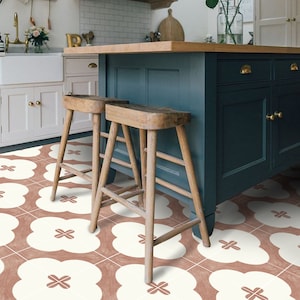 Op de afbeelding: Twee houten barstoelen met een teal keukeneiland op de achtergrond. De vloer is betegeld met een wit en roze geometrisch patroon.