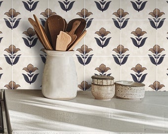 May include: A white ceramic jar filled with wooden kitchen utensils stands on a countertop. The background features a tiled wall with a repeating floral pattern in brown, navy, and cream. Two small ceramic bowls are also on the countertop.