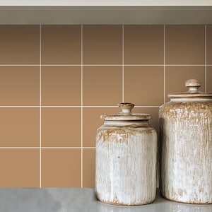 Op de afbeelding: Twee keramische potten met deksels, één bruin en één wit, op een bruine betegelde aanrecht.