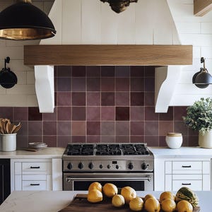 Puede incluir: Una cocina moderna con una estufa de gas de acero inoxidable, gabinetes blancos y una campana extractora de madera. El salpicadero presenta azulejos cuadrados de color burdeos. Una tabla de madera contiene limones y un melón.