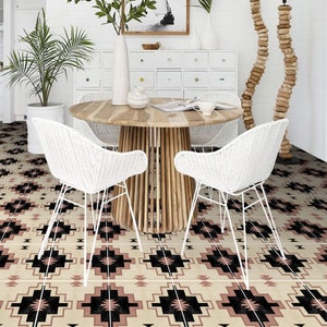 May include: A white dining table with a wooden top and a white wicker chair on each side. The table is set with a bowl and a book. The floor is tiled with a black, white and pink geometric pattern.