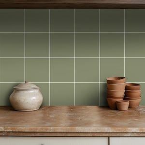 May include: A kitchen countertop with a green tiled backsplash and a white ceramic jar and a stack of terracotta pots.