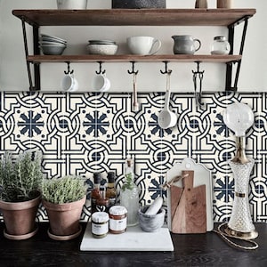 Pode incluir: Um backsplash de cozinha com um padrão de ladrilho geométrico preto e branco. Os ladrilhos apresentam um design repetitivo de círculos e estrelas entrelaçados. O backsplash é acentuado por uma prateleira de madeira com ganchos e vários itens de cozinha.