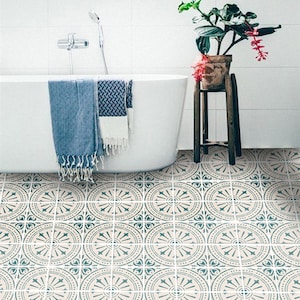 May include: A bathroom with a white bathtub and a plant in a brown pot on a wooden stand. The floor is tiled with a geometric pattern in shades of blue and beige.