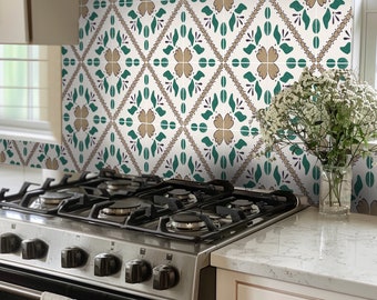 Puede incluir: Azulejos decorativos para salpicadero de cocina con un patrón repetido de hojas verdes, flores marrones y detalles morados sobre un fondo blanco. Los azulejos están instalados sobre una estufa de gas de acero inoxidable y una encimera blanca.