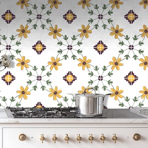 May include: A white kitchen backsplash with a repeating pattern of yellow flowers and green leaves. The backsplash is behind a stainless steel pot on a black hob.