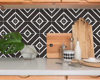 Puede incluir: Salpicadero de azulejos geométricos en blanco y negro con un patrón de diamantes blancos. El salpicadero está instalado en una cocina con armarios y encimeras de madera. Hay varios utensilios de cocina y accesorios en la encimera, incluyendo tablas de cortar, un jarrón con una planta verde y una botella de aceite.