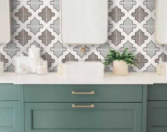 May include: A bathroom vanity with three drawers and gold handles. The vanity is painted a teal green color. The backsplash is white tile with a geometric pattern in brown and gray.