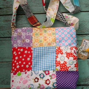 May include: A patchwork shoulder bag with a variety of colorful fabric squares. The bag features a long strap made of different patterned fabrics. The bag is on a turquoise wooden surface. A tag with text hangs from the bag.