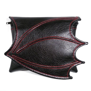 Peut inclure: Pochette en cuir noir avec des coutures rouges en forme d'aile de chauve-souris.