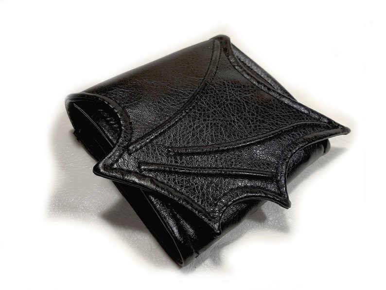 May include: A black leather wallet shaped like a bat wing. The wallet is folded closed and the bat wing design is prominent.