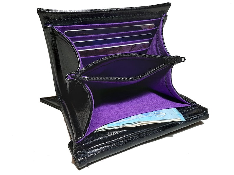 May include: Black leather wallet with a purple interior. The wallet has multiple card slots and a zippered compartment. The wallet is open and there is a bill inside.