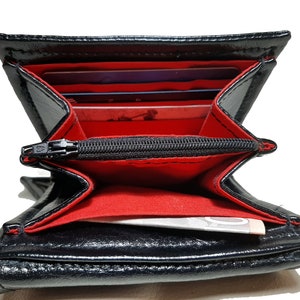May include: Black leather wallet with a red interior and a zippered pocket. The wallet is open and shows multiple card slots and a bill compartment.