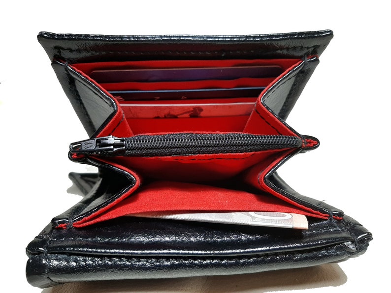 May include: Black leather wallet with a red interior and a zippered pocket. The wallet is open and shows multiple card slots and a bill compartment.