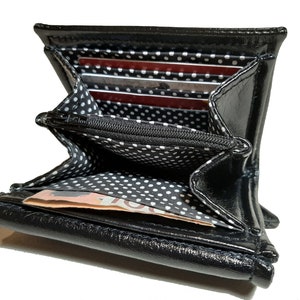 May include: Black leather wallet with a white polka dot lining. The wallet is open and has several card slots and a bill compartment.