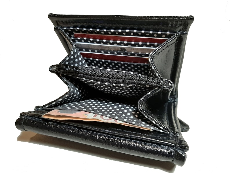 May include: Black leather wallet with a white polka dot lining. The wallet is open and has several card slots and a bill compartment.