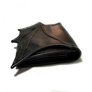 May include: A black leather wallet with a bat wing design. The wallet is folded closed and the bat wing design is visible on the front.