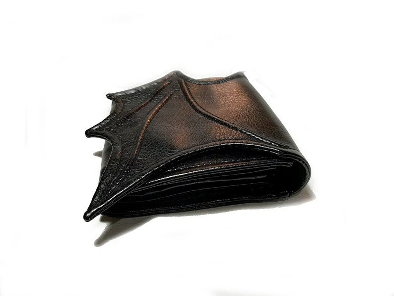 May include: A black leather wallet with a bat wing design. The wallet is folded closed and the bat wing design is visible on the front.