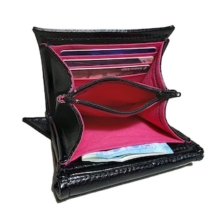 May include: Black leather wallet with a pink interior and a zippered pocket. The wallet is open and shows several credit cards and cash inside.