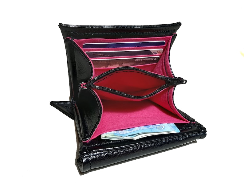 May include: Black leather wallet with a pink interior and a zippered pocket. The wallet is open and shows several credit cards and cash inside.