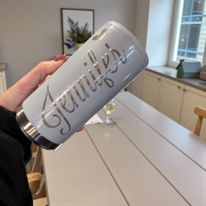 Op de afbeelding: Lichtblauwe geïsoleerde beker met de naam "Jennifer" in sierlijke letters. De beker heeft een zilveren rand en een hartvormige uitsparing. Ontworpen om dranken koud of warm te houden. Ideaal voor onderweg.