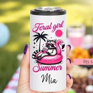Könnte beinhalten: Weißer schlanker Dosenkühler mit schwarzem Deckel, mit einem Waschbären mit Sonnenbrille auf einem rosa Flamingo-Schwimmer. Der Text lautet "Feral girl Summer Mia". Der Kühler ist für schlanke Dosen geeignet.
