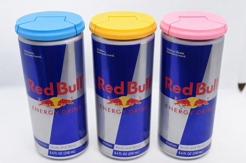Puede incluir: Tres latas de bebida energ&eacute;tica Red Bull con tapas azules, amarillas y rosas. Cada lata tiene un dise&ntilde;o plateado y azul con el logotipo de Red Bull y el texto "ENERGY DRINK". Cada lata contiene 250 ml.