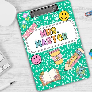 Puede incluir: Un portapapeles verde con un borde blanco y una funda de pl&aacute;stico transparente. El portapapeles tiene una variedad de pegatinas e ilustraciones coloridas, incluyendo una cara sonriente, una taza de caf&eacute;, un l&aacute;piz y un libro. El texto "Mrs. Master" est&aacute; escrito en letras de colores en el portapapeles.