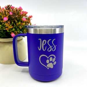 Peut inclure: Une tasse à café en acier inoxydable de couleur violette avec une anse. La tasse a une empreinte de patte à l'intérieur d'un cœur et le nom "Jess" gravé sur le devant.