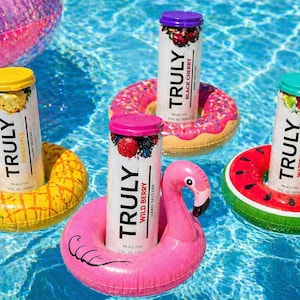 Puede incluir: Cuatro latas de Truly Hard Seltzer flotando en una piscina, cada una en un portavasos inflable diferente. Los sabores incluyen Pi&ntilde;a, Cereza Negra, Baya Silvestre y Sand&iacute;a Lima. Los portavasos tienen forma de pi&ntilde;a, donut, flamenco y rodaja de sand&iacute;a.