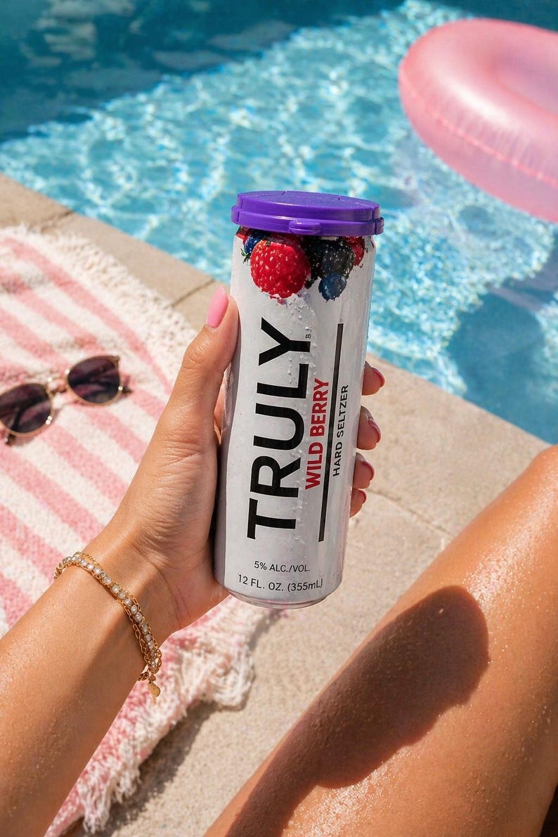 Puede incluir: Una lata de Truly Wild Berry Hard Seltzer con tapa morada y dise&ntilde;o de bayas. La lata es sostenida por una persona cerca de una piscina. La lata dice "TRULY WILD BERRY HARD SELTZER" y "5% ALC./VOL. 355ml".