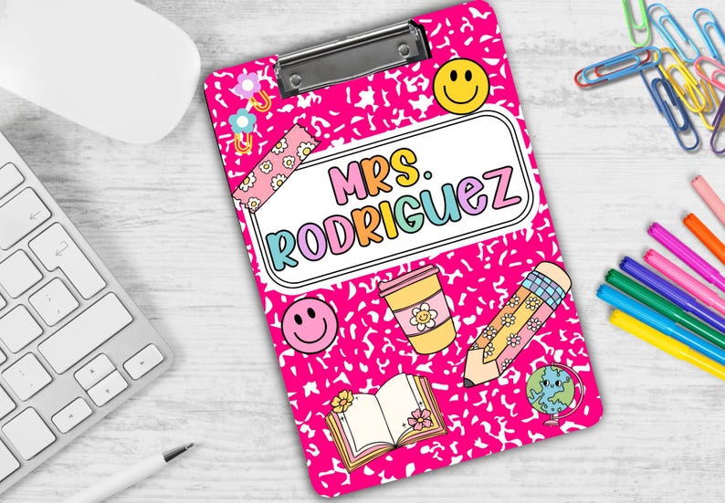 Puede incluir: Portapapeles rosa con un dise&ntilde;o estampado blanco y negro. El portapapeles tiene una funda de pl&aacute;stico transparente y un clip de metal. El portapapeles tiene una pegatina blanca con el texto "Mrs. Rodriguez" en letras de arco&iacute;ris. El portapapeles tambi&eacute;n tiene varias pegatinas, incluyendo una cara sonriente, un l&aacute;piz, una taza de caf&eacute;, un libro y un globo terr&aacute;queo.