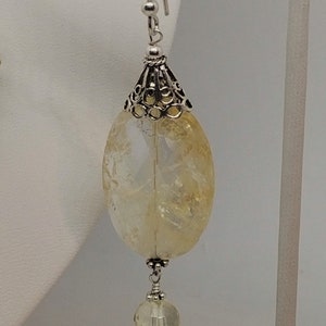 Puede incluir: Pendientes de plata con una piedra preciosa de citrino amarillo y una perla de cristal transparente.