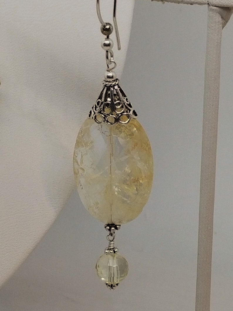 Puede incluir: Pendientes de plata con una piedra preciosa de citrino amarillo y una perla de cristal transparente.