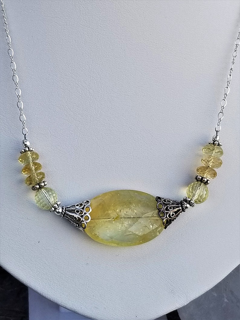 Puede incluir: Un collar de cadena de plata con un gran colgante de citrino amarillo y cuentas de citrino amarillo m&aacute;s peque&ntilde;as. El colgante est&aacute; engastado en un marco de filigrana de plata.