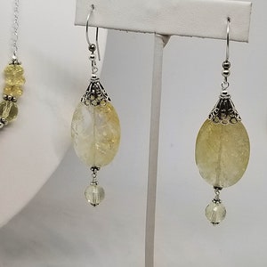 Puede incluir: Un par de pendientes de plata con piedras de citrino amarillo y detalles de cristal transparente. Los pendientes est&aacute;n colgados de un soporte de plata.