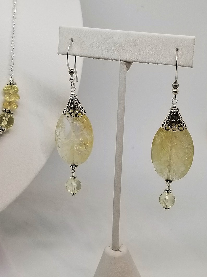Puede incluir: Un par de pendientes de plata con piedras de citrino amarillo y detalles de cristal transparente. Los pendientes est&aacute;n colgados de un soporte de plata.
